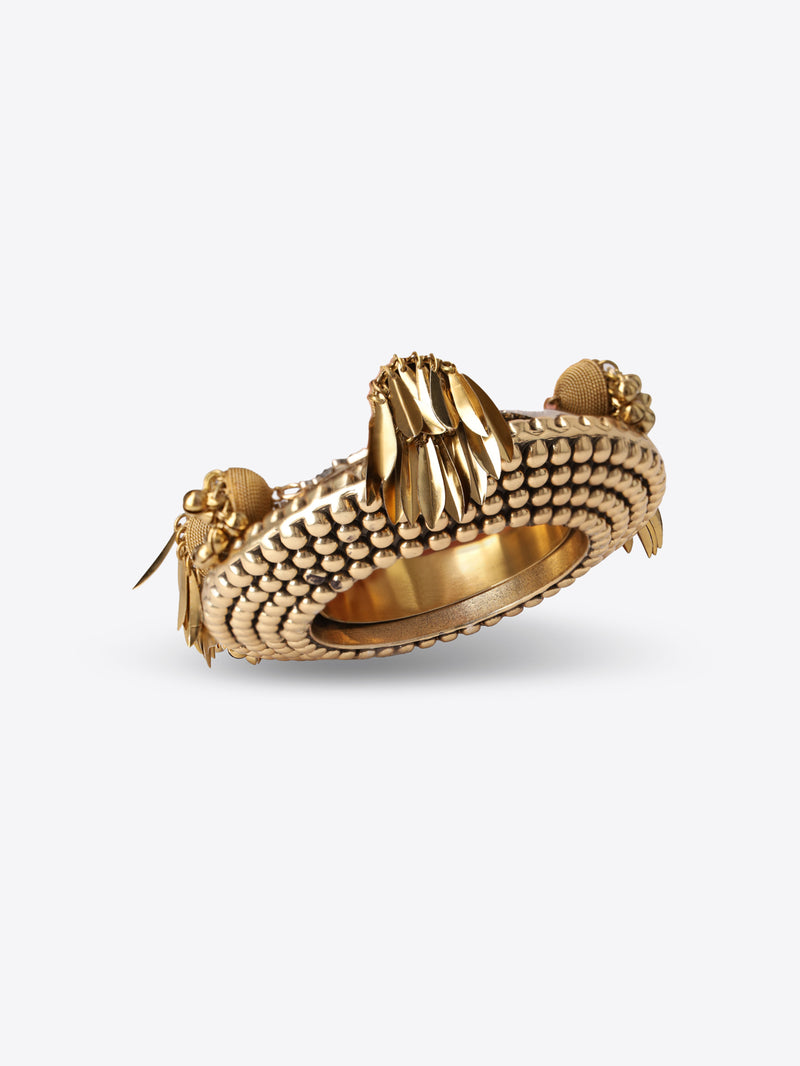 Ornate old brass cuff bracelet with a textured beaded surface, silver-toned edging, and dangling leaf and bead charms on a light gray background.