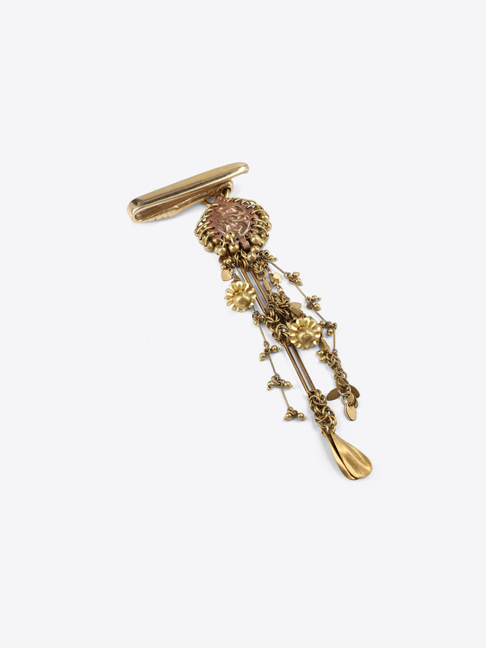 Back view of a gold-toned flower-shaped button cover, showing its fastening mechanism on a light gray background.