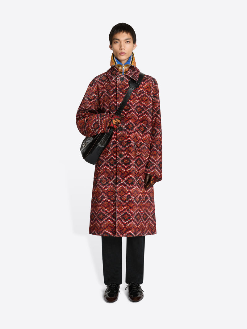 Person wearing a patterned long coat, floral patterned gloves, holding a black bag on a white background