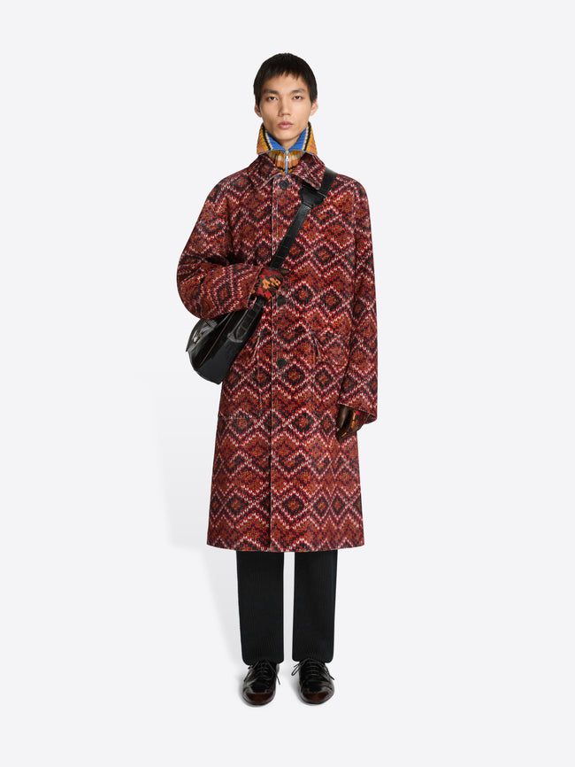 Person wearing a patterned coat, holding a black bag on a white background