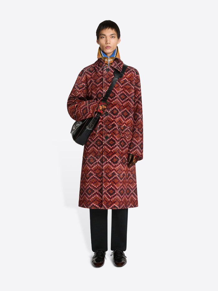 Person wearing a patterned coat, holding a black bag on a white background
