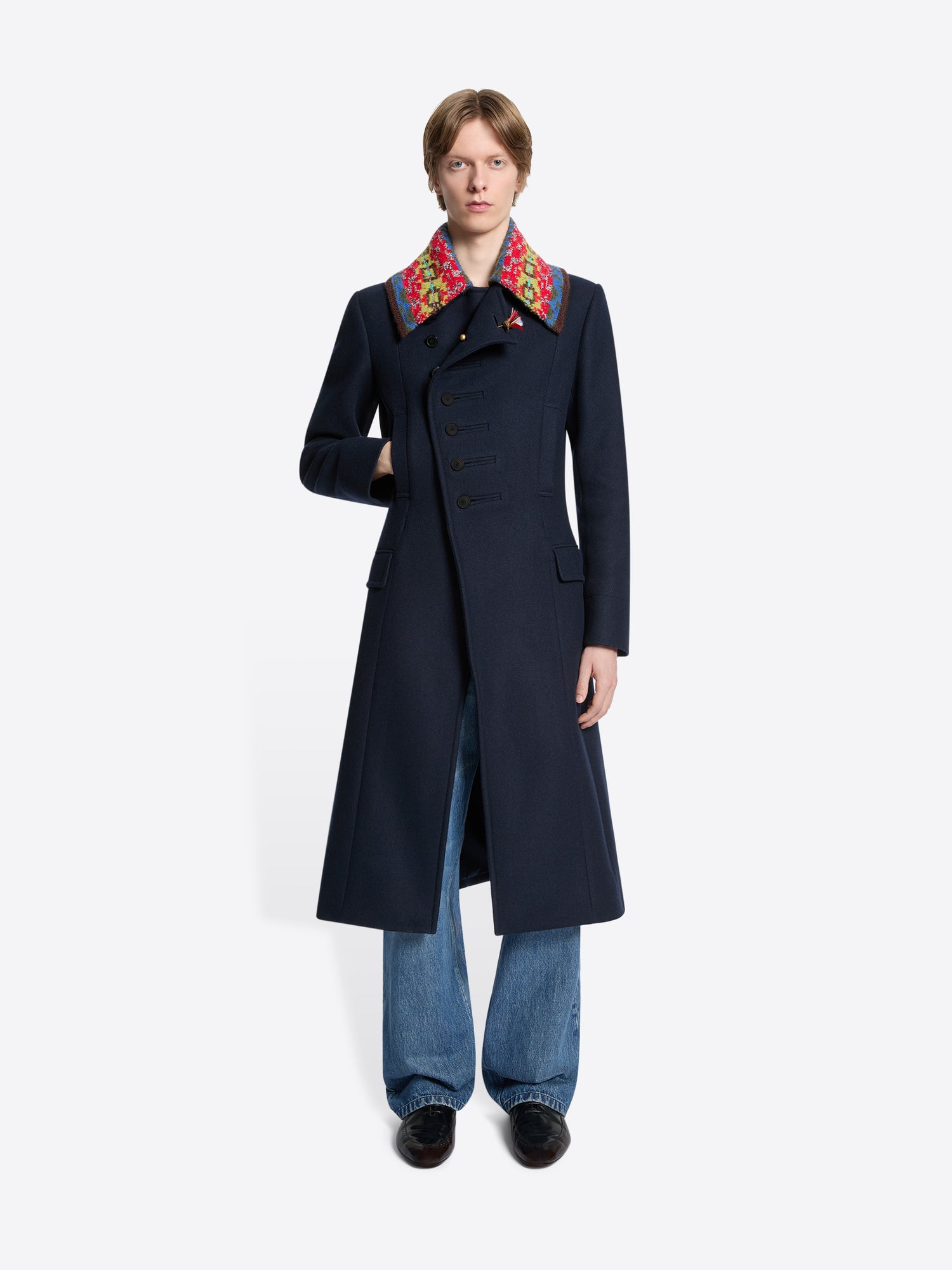 Person wearing a long dark coat with colorful collar on a white background