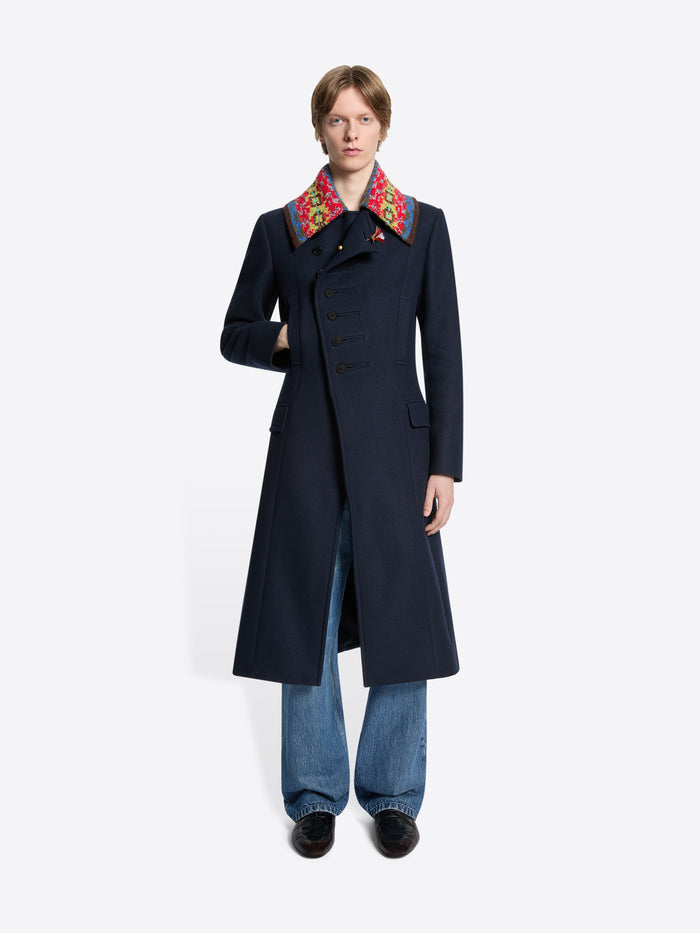 Person wearing a long dark coat with colorful collar on a white background