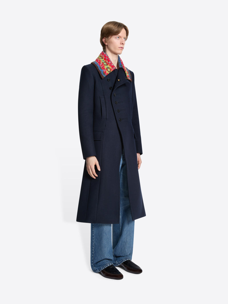 Person wearing a long dark coat with a colorful collar on a white background