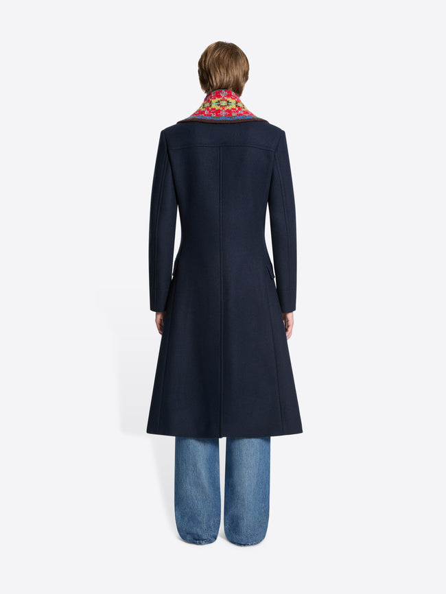 Back view of a person wearing a navy coat with a colorful patterned collar on a white background