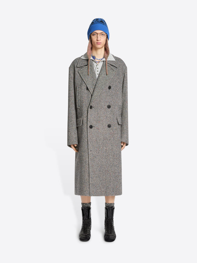 Person wearing a gray coat, blue hat, and black boots on a white background