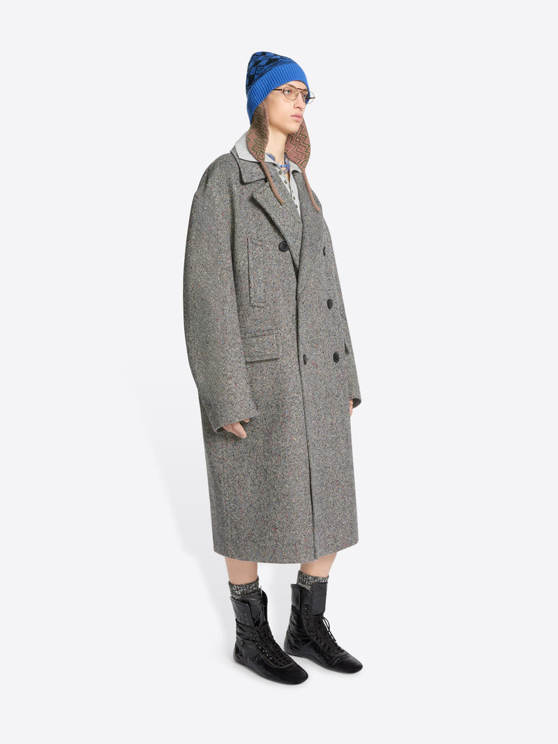 Person wearing a long gray coat, blue hat, and black boots on a white background