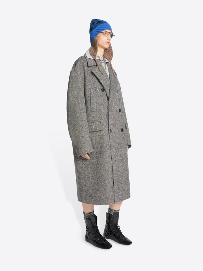 Person wearing a long gray coat, blue hat, and black boots on a white background
