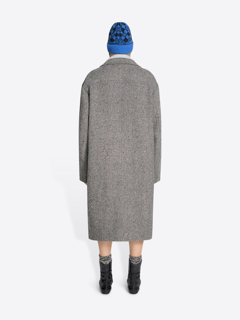 Back view of a person wearing a gray coat and blue beanie on a white background