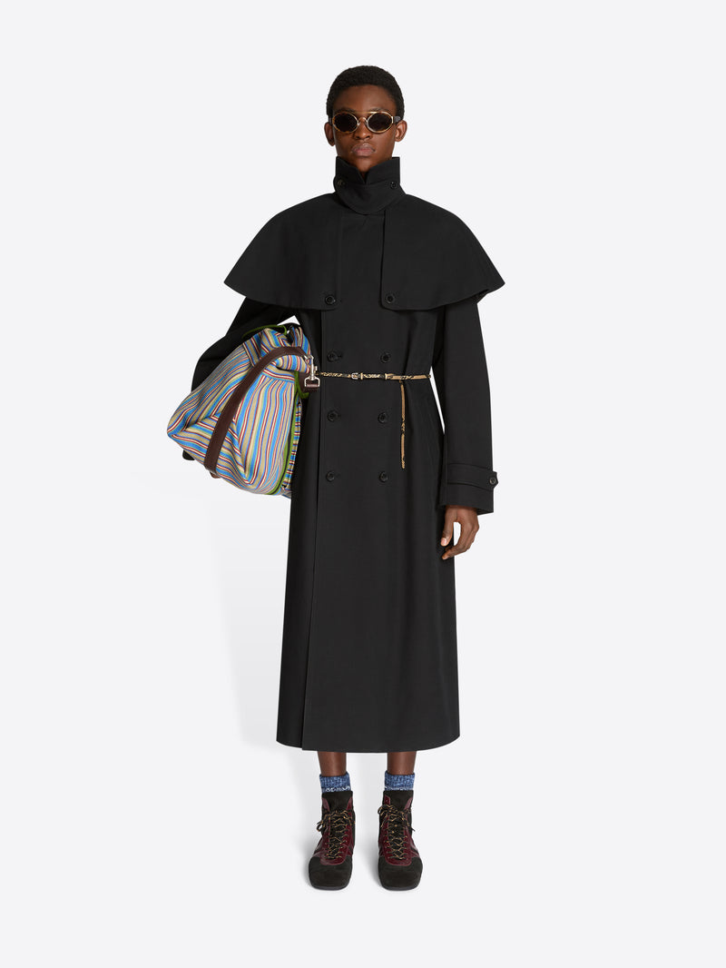 Person wearing a long black coat with a colorful bag on a white background