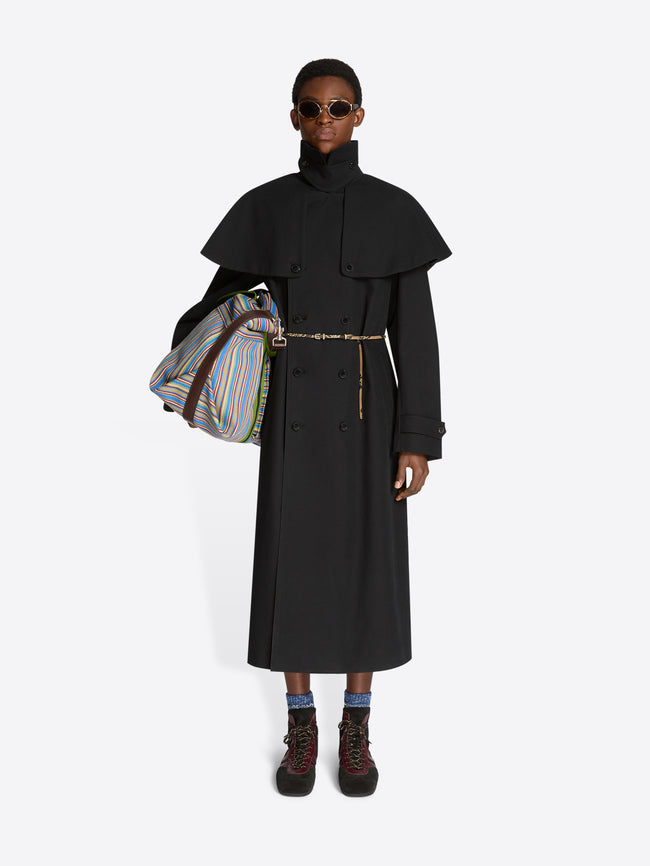 Person wearing a long black coat with a colorful bag on a white background