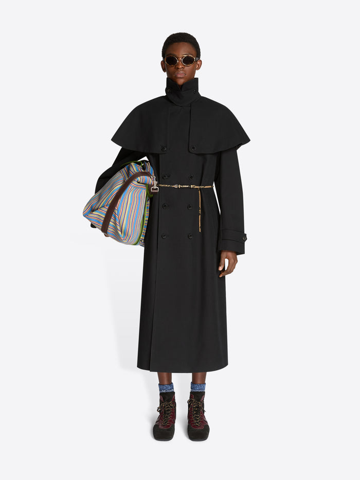 Person wearing a long black coat with a colorful bag on a white background