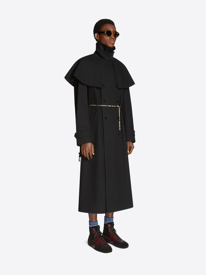 Person wearing a long black coat with a belt on a white background