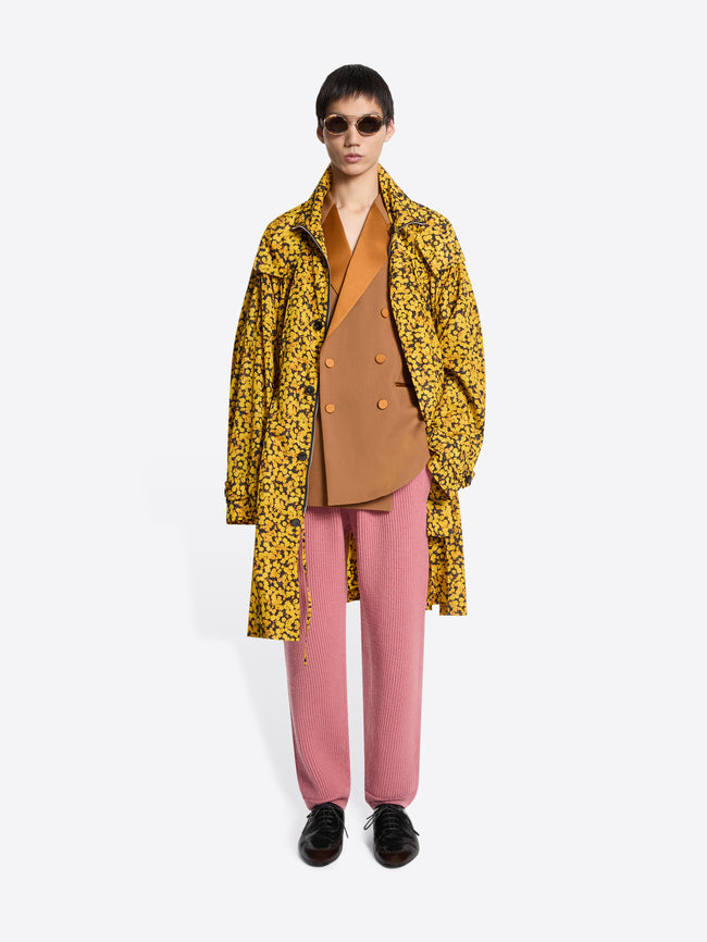 Person wearing a yellow floral coat, orange blazer, pink pants, and brown shoes on a white background
