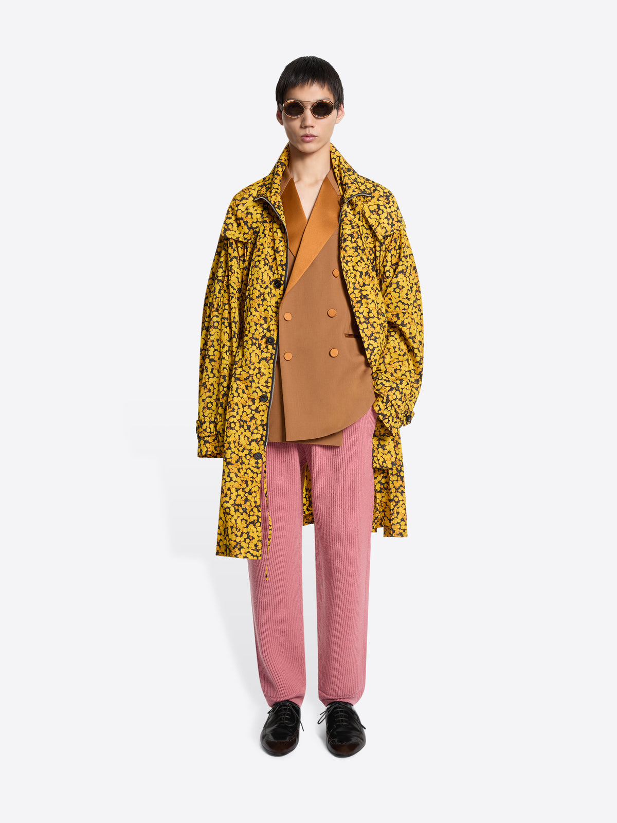 Person wearing a yellow floral coat, orange blazer, pink pants, and brown shoes on a white background