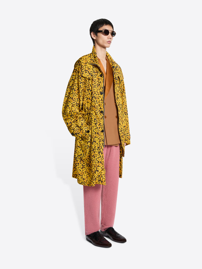 Person wearing a yellow floral coat, pink pants, and brown shoes on a white background