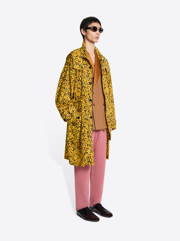 Person wearing a yellow floral coat, pink pants, and brown shoes on a white background