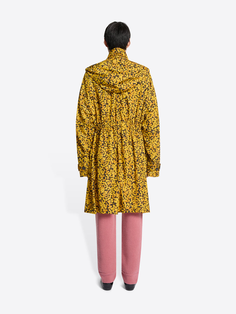 Back view of a person wearing a yellow floral coat, pink pants, and brown shoes on a white background