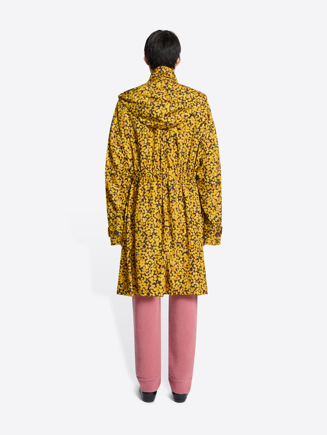 Back view of a person wearing a yellow floral coat, pink pants, and brown shoes on a white background