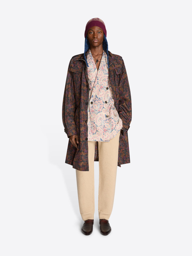 Person wearing a patterned floral coat, floral shirt, hat and beige pants on a white background