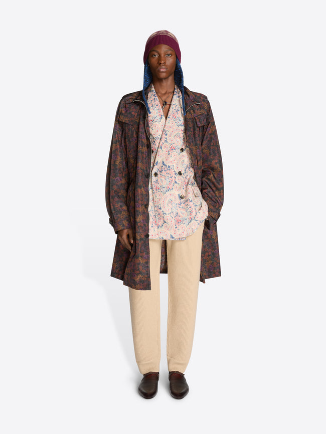 Person wearing a patterned floral coat, floral shirt, hat and beige pants on a white background
