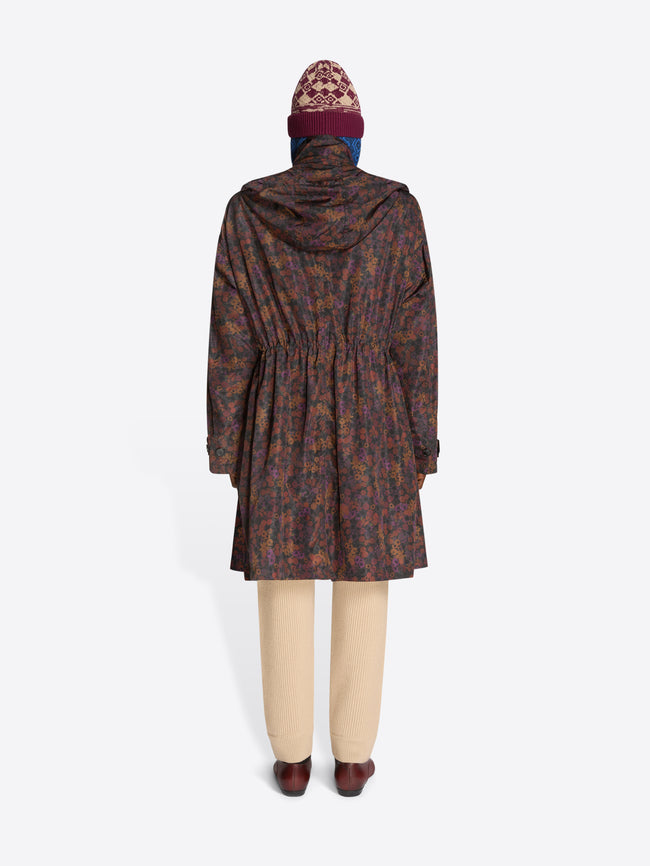Back view of a person wearing a patterned floral coat, hat and beige pants on a white background