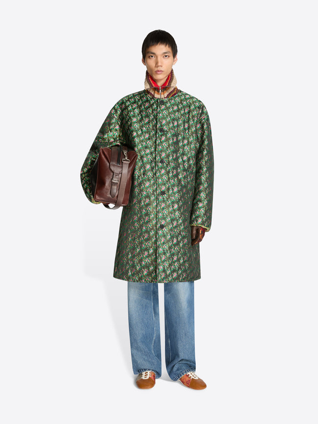 Person wearing a green patterned coat holding a brown bag on a white background