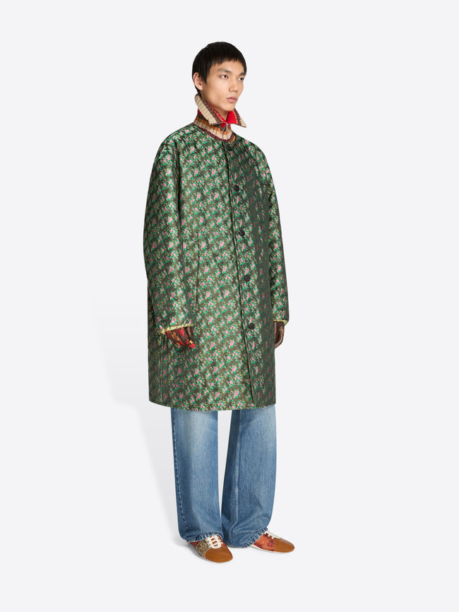 Person wearing a green patterned coat and blue jeans on a white background