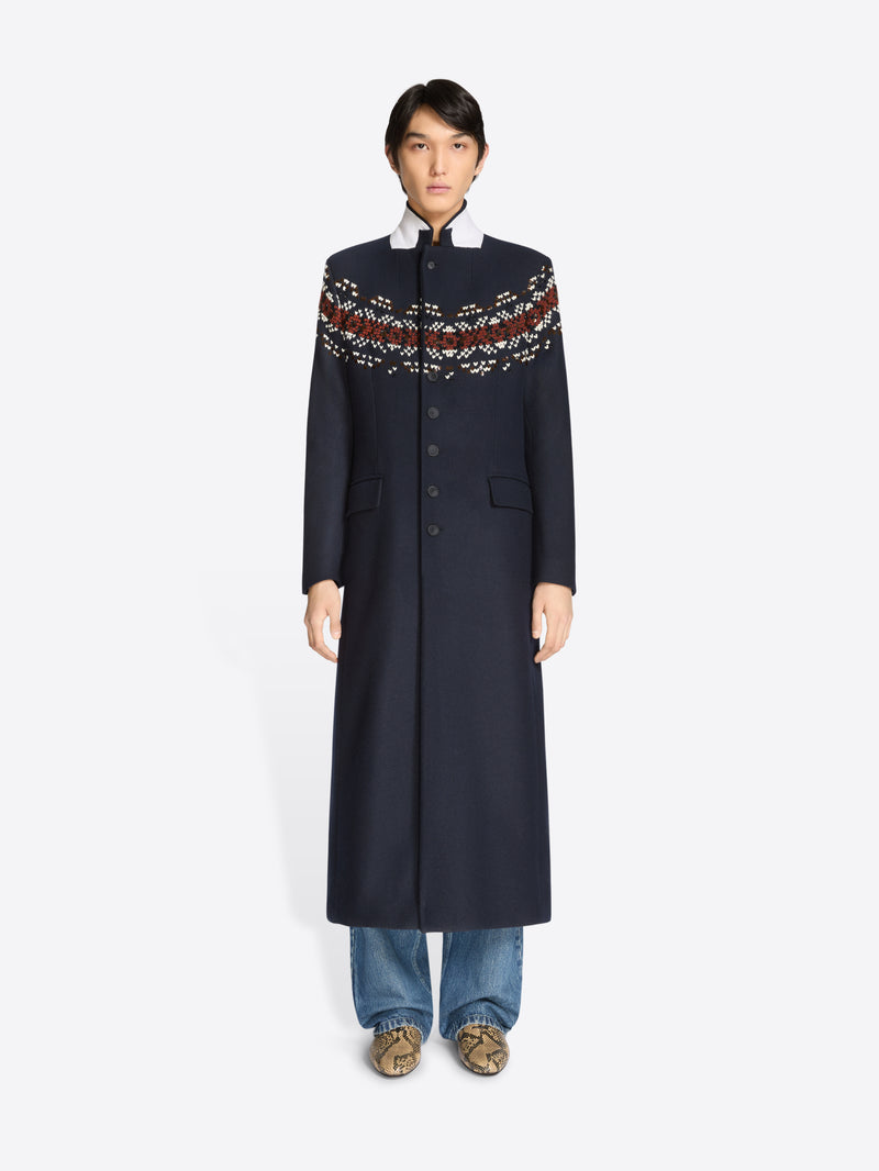 Person wearing a long navy coat with patterned sleeves on a white background 