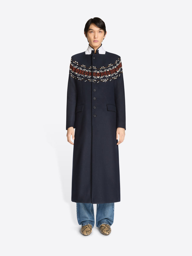 Person wearing a long navy coat with patterned sleeves on a white background 
