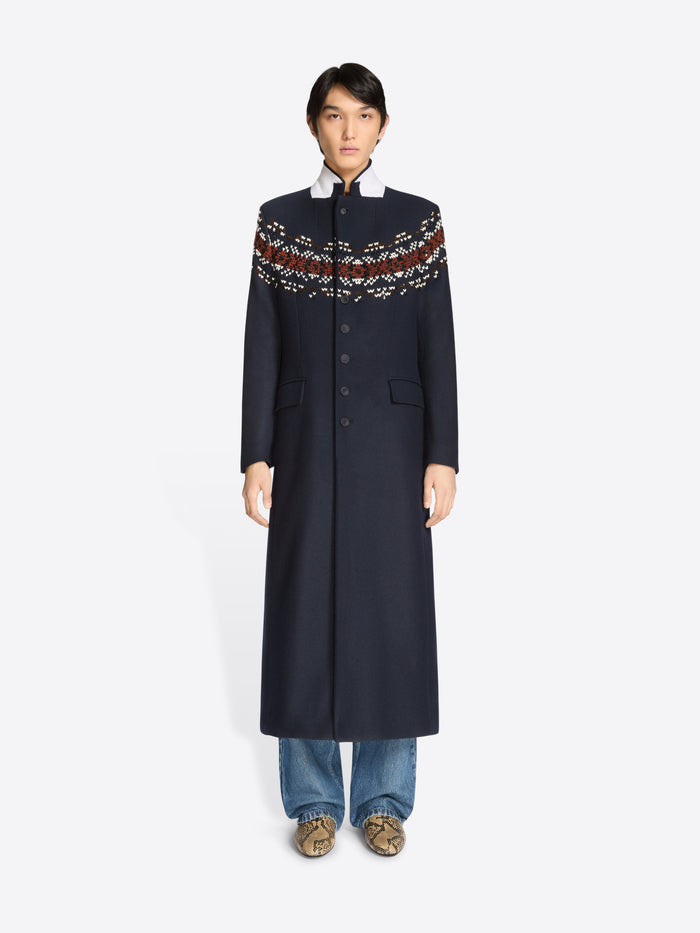 Person wearing a long navy coat with patterned sleeves on a white background 