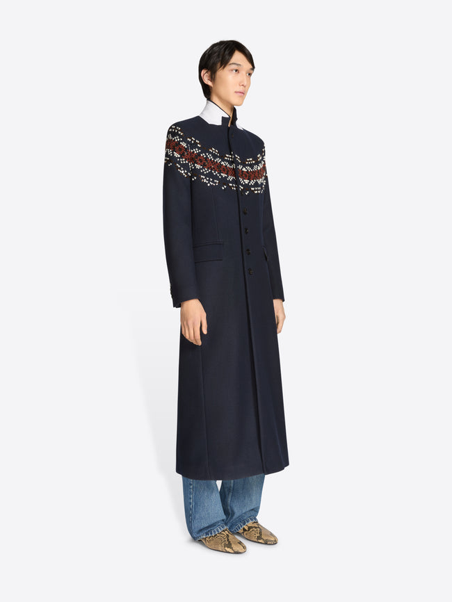 Person wearing a long navy coat with patterned sleeves on a white background 