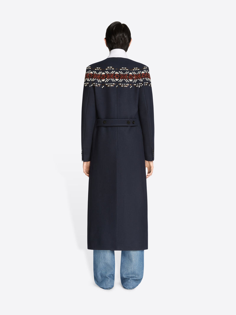 Back view of a person wearing a long navy coat with patterned sleeves on a white background 