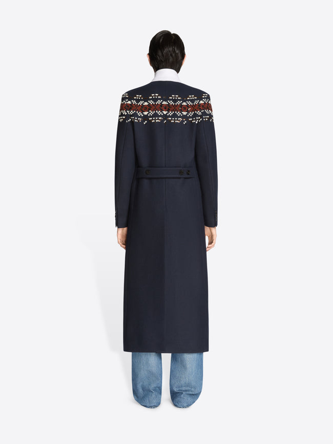 Back view of a person wearing a long navy coat with patterned sleeves on a white background 