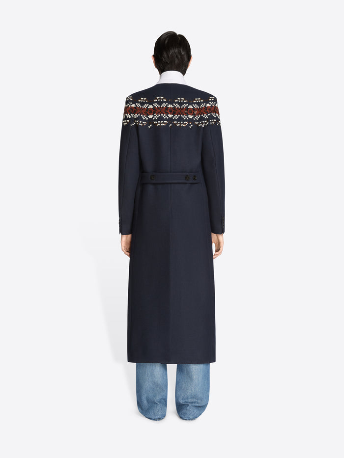 Back view of a person wearing a long navy coat with patterned sleeves on a white background 