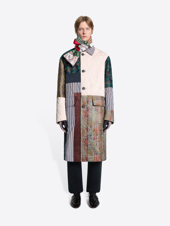 Person wearing a patchwork coat with a colorful scarf on a white background