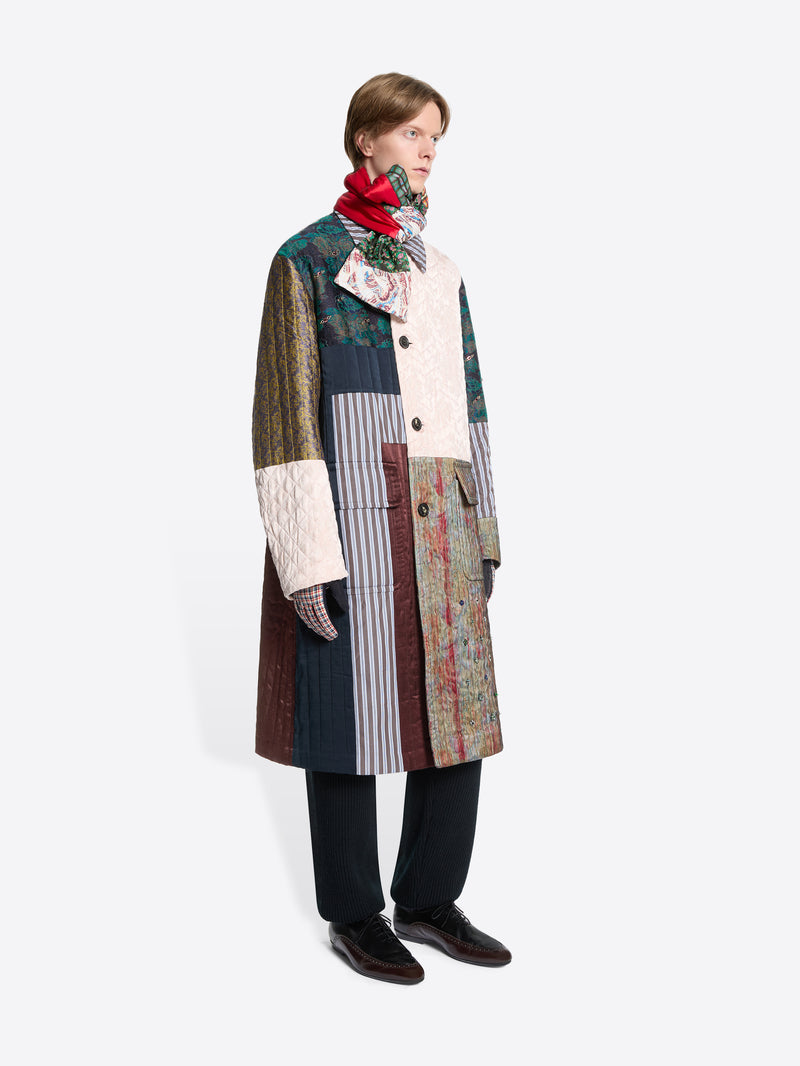 Person wearing a patchwork coat with a colorful scarf on a white background