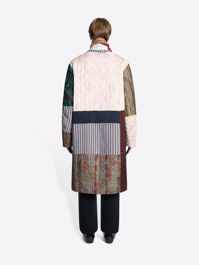 Back view of a person wearing a patchwork coat with a colorful scarf on a white background