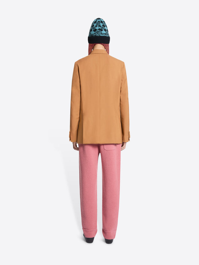 Back view of a person wearing an orange blazer, pink pants, and a patterned hat on a white background