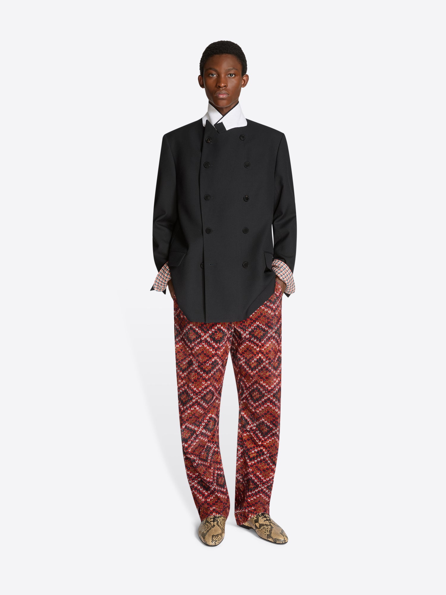 Person wearing a black blazer and red patterned pants on a white background