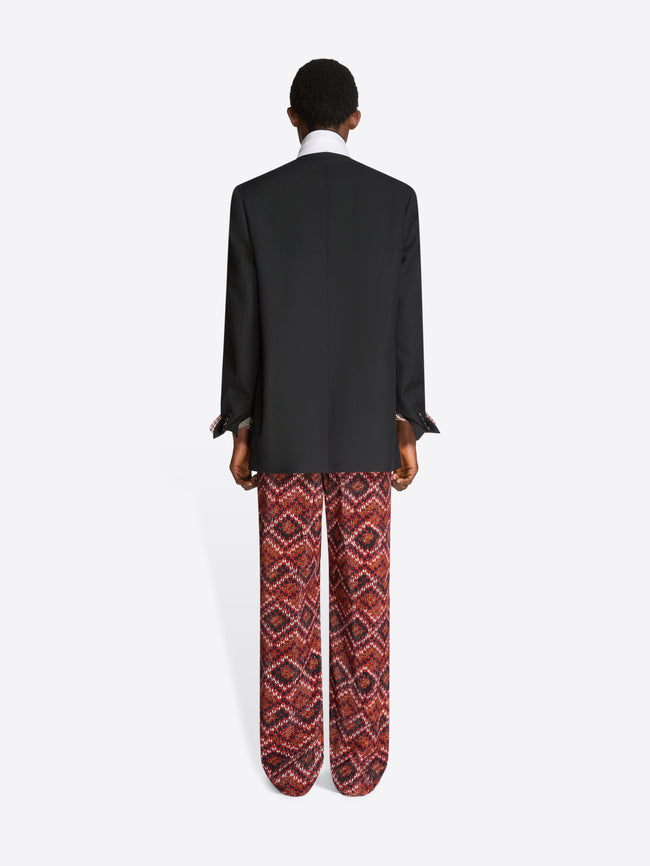 Back view of a person wearing a black blazer and patterned pants on a white background