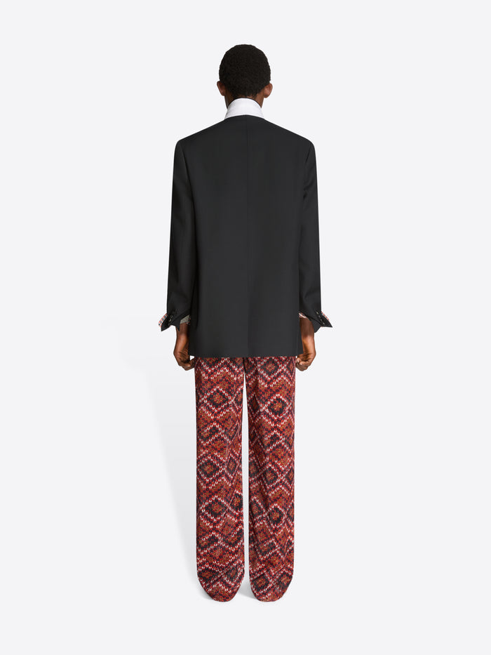 Back view of a person wearing a black blazer and patterned pants on a white background