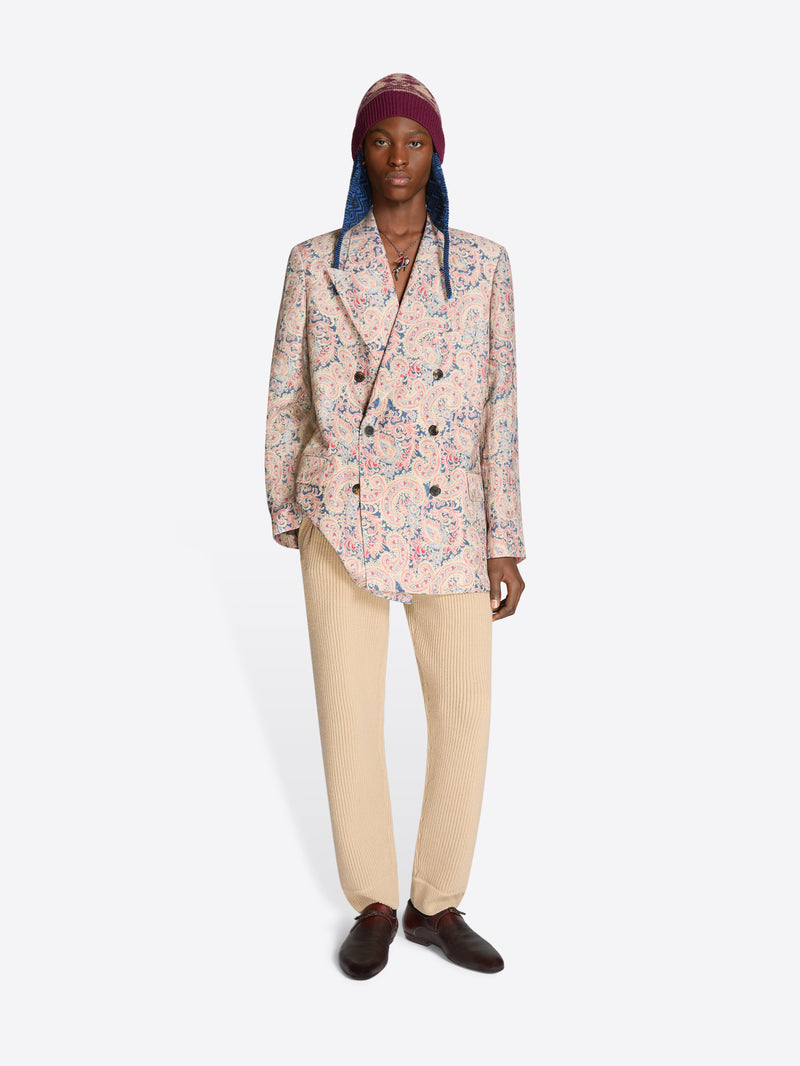 Person wearing a floral blazer, beige pants and a patterned hat on a white background