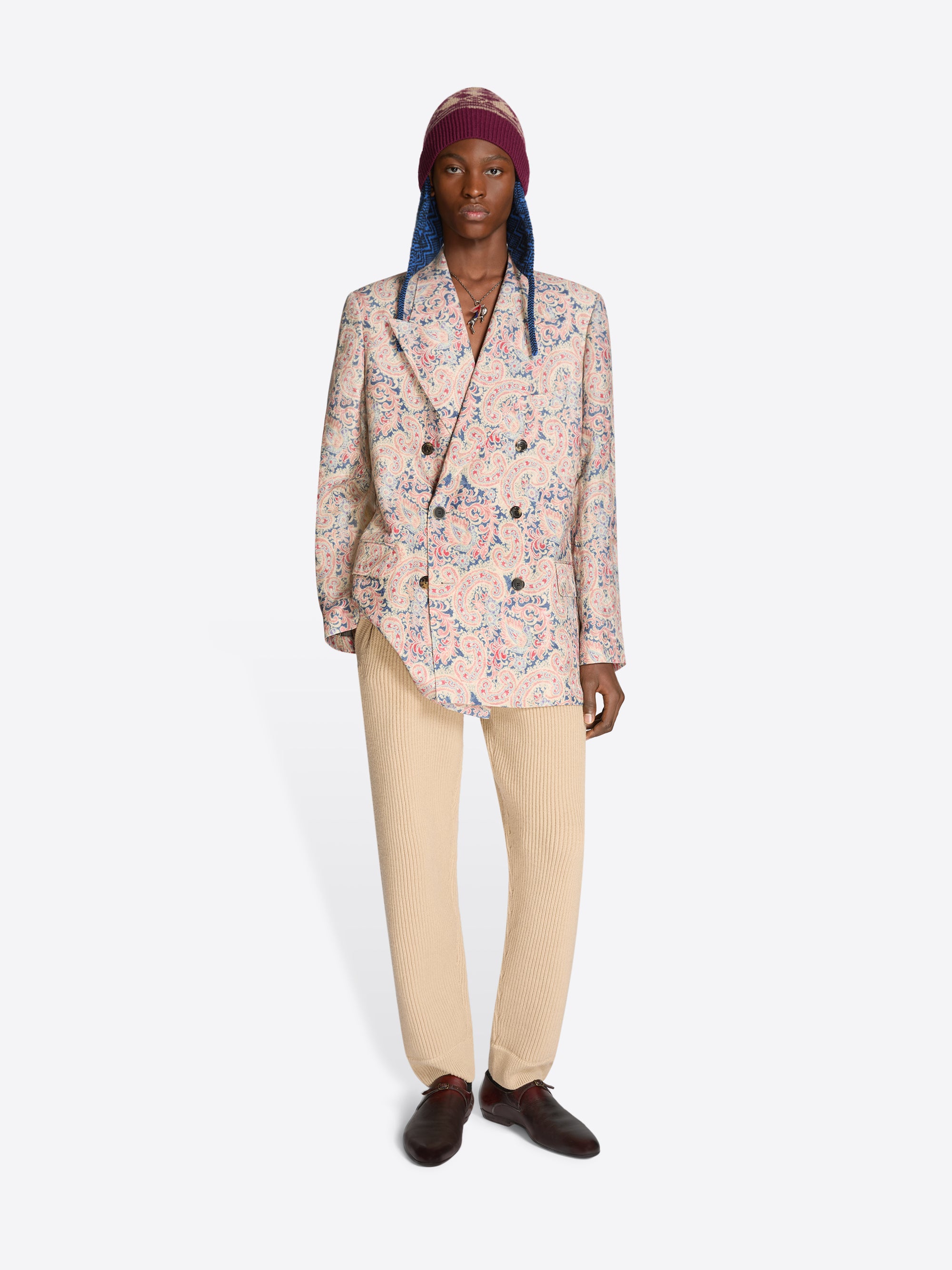 Person wearing a floral blazer, beige pants and a patterned hat on a white background