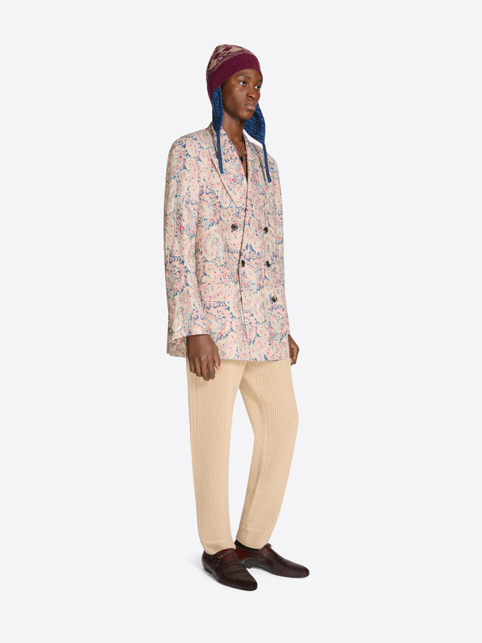 Person wearing a patterned floral blazer, beige pants, and a patterned hat on a white background