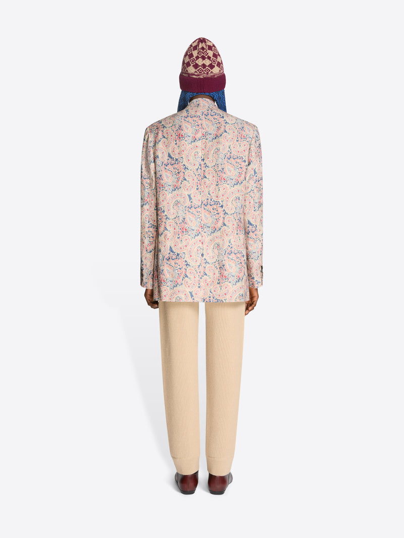 Back view of a person wearing a floral blazer, beige pants and a patterned hat on a white background