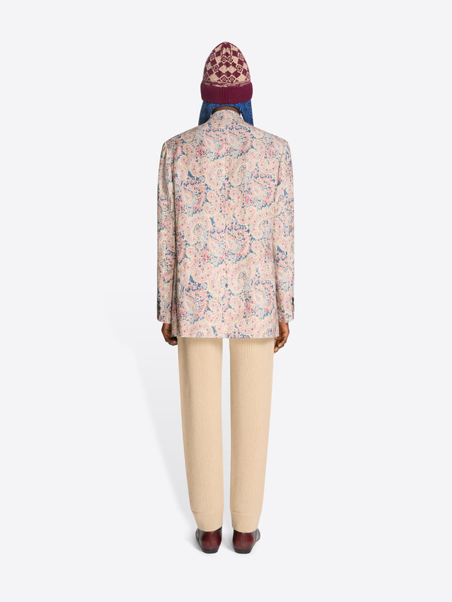 Back view of a person wearing a floral blazer, beige pants and a patterned hat on a white background