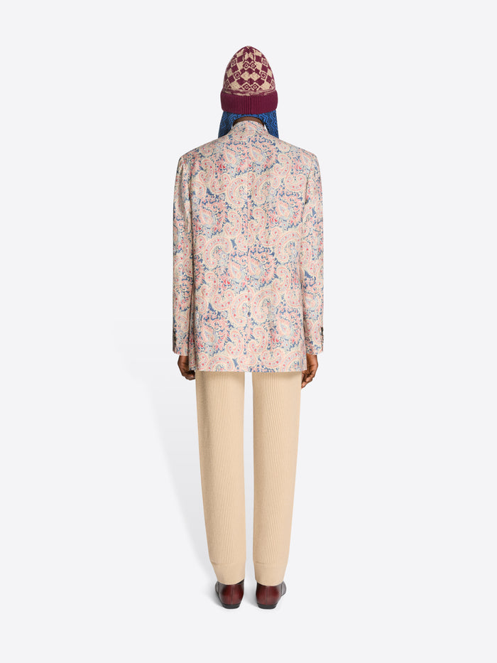 Back view of a person wearing a floral blazer, beige pants and a patterned hat on a white background