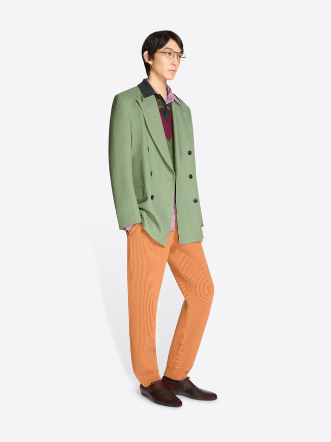 Person wearing a green blazer and orange pants on a white background
