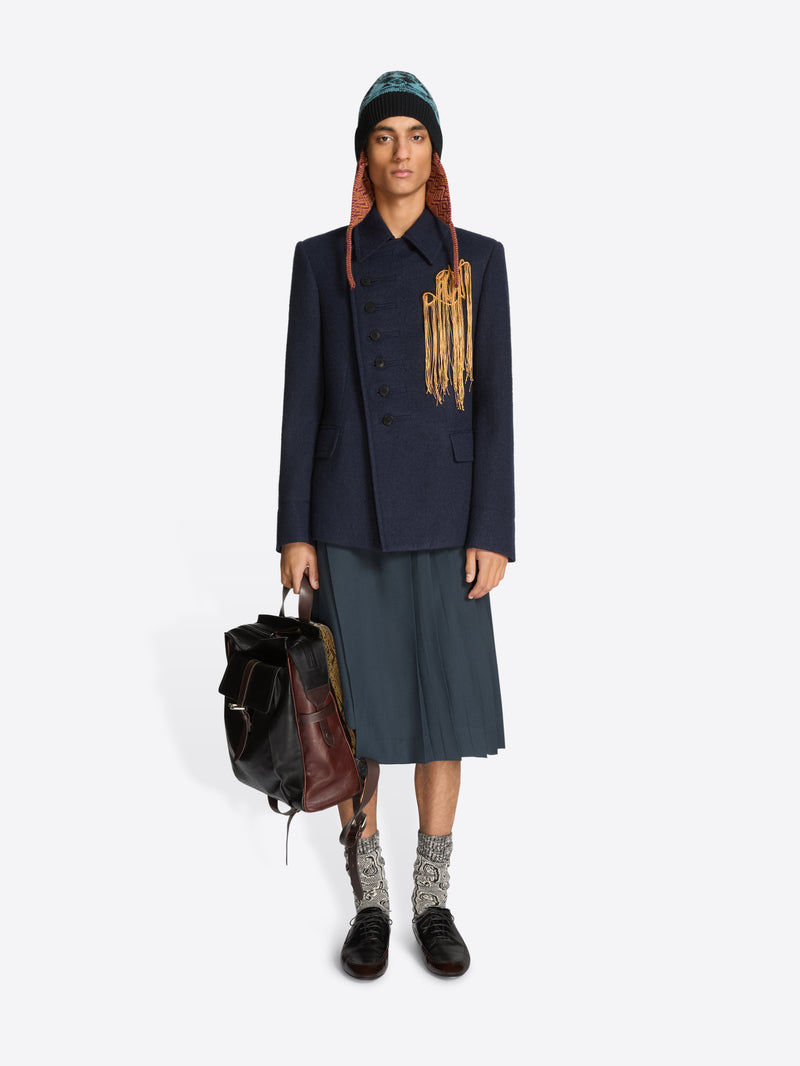 Person wearing a dark coat, skirt, and black shoes holding a backpack on a white background